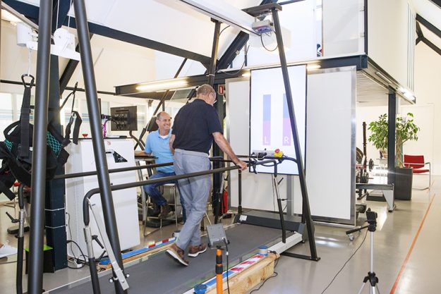 Man met etalagebenen wordt door de fysiotherapeut geholpen door middel van looptherapie