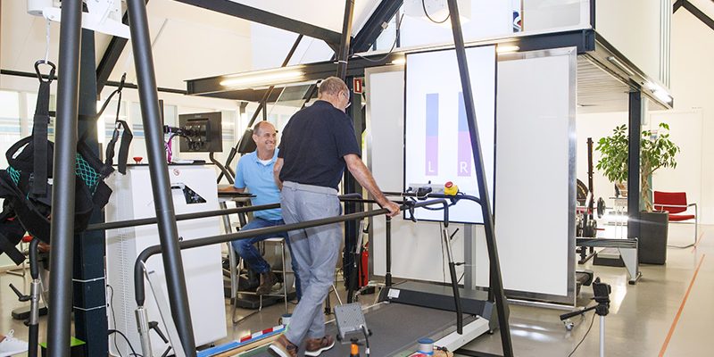 Man met etalagebenen wordt door de fysiotherapeut geholpen door middel van looptherapie