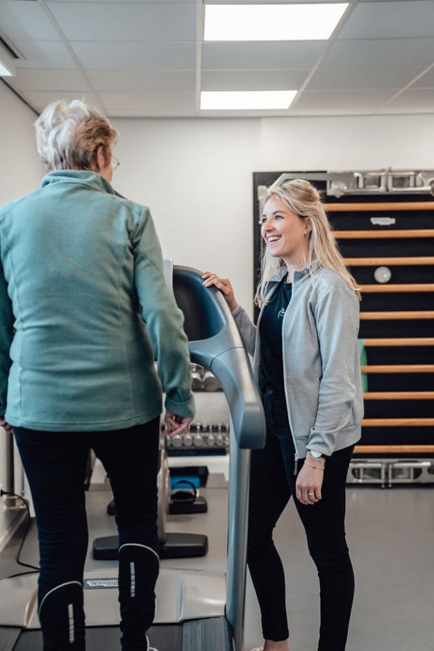 Mevrouw van Duin heeft artrose en loopt op de loopband onder begeleiding van Fysiotherapeut Laura in de oefenzaal.