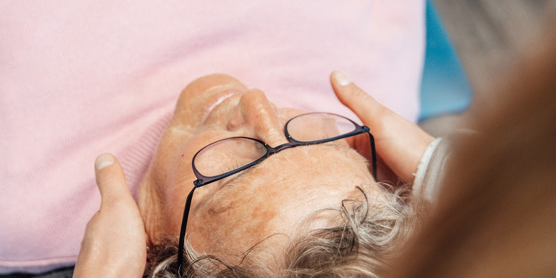 Vrouw in een roze shirt met bril op probeert met behulp van de fysiotherapie te slapen en haar hoofdpijn te verhelpen.