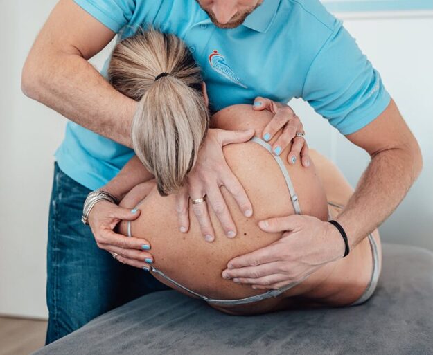Manueel therapeut in een blauwe polo helpt een patiënt zonder shirt door middel van manuele therapie in Lienden bij chronische lage rugklachten en door de rug gaan.