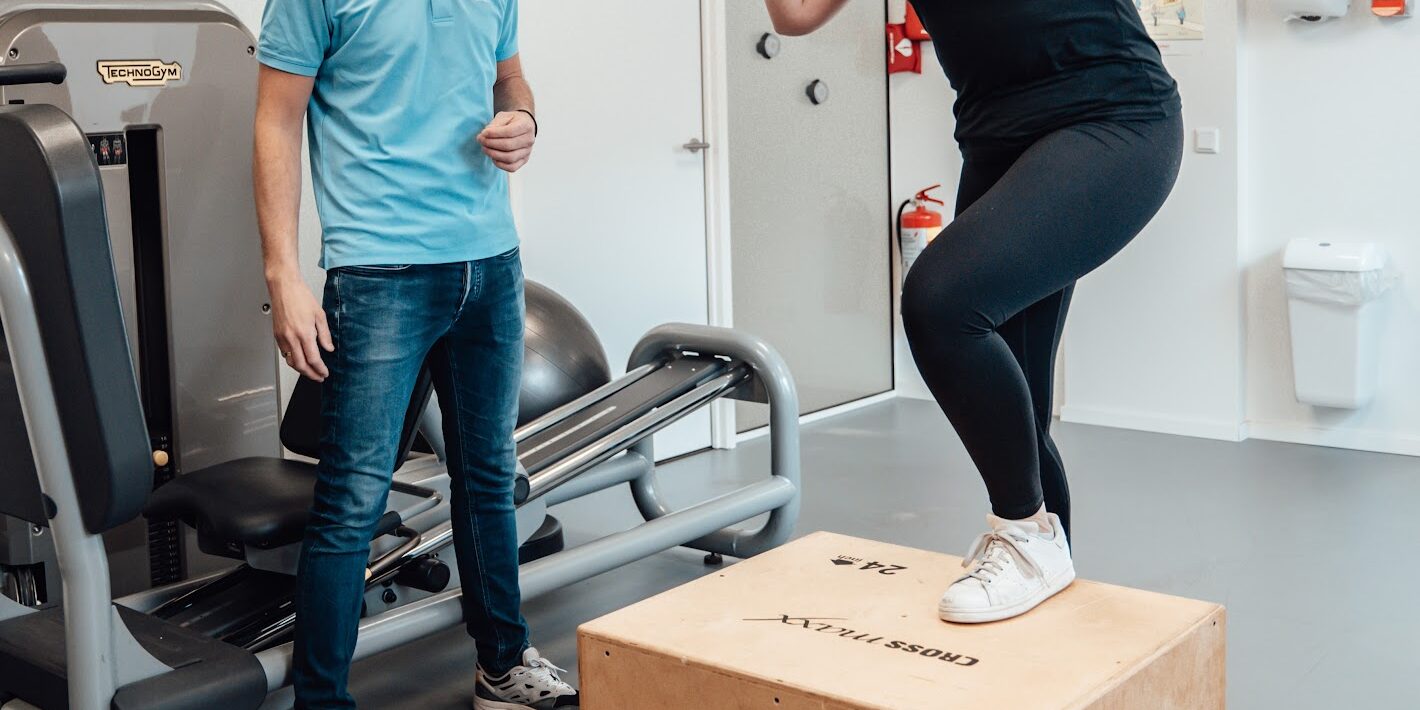 blessure Vrouwelijke patiënt in zwarte kleding werkt weer aan de opbouw van haar spierkracht na het oplopen van een blessure met behulp van een fysiotherapeut in een blauwe polo