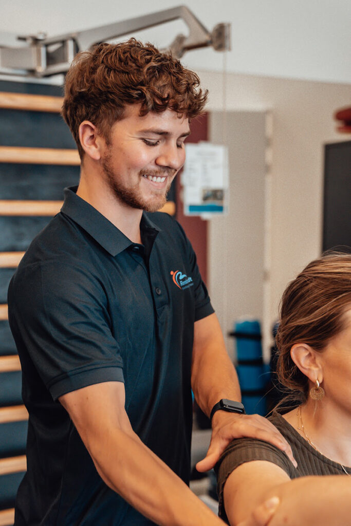 Fysiotherapeut in een donkerblauw shirt helpt een patiënt die niet een schouderoperatie heeft gehad