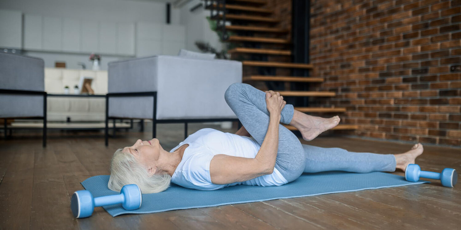 knakkende knieën vrouw werkt aan haar knakkende knieën door oefeningen te doen in haar woonkamer op een yogamat.